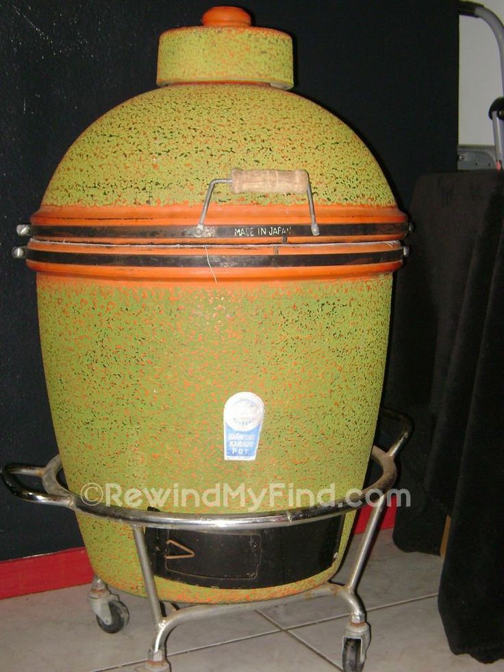 a large green and orange pot sitting on top of a metal cart next to a black wall