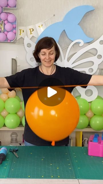 a woman is holding an orange balloon in front of her face while standing next to balloons