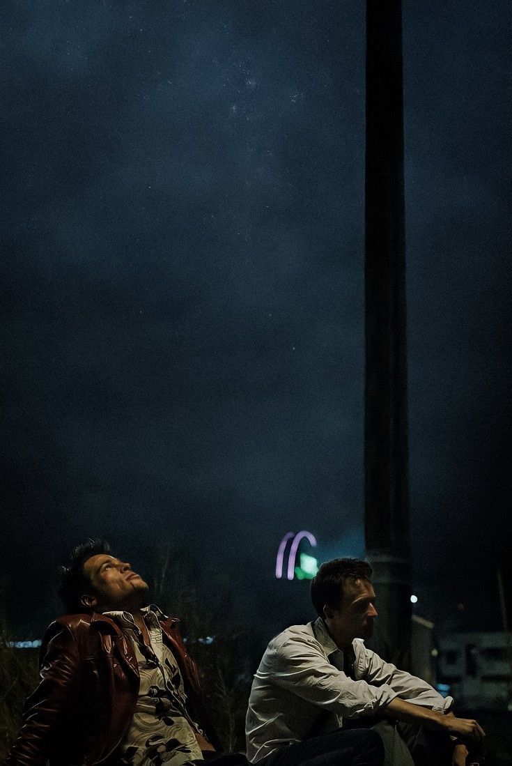 two men sitting on the ground at night with their eyes closed and one looking up