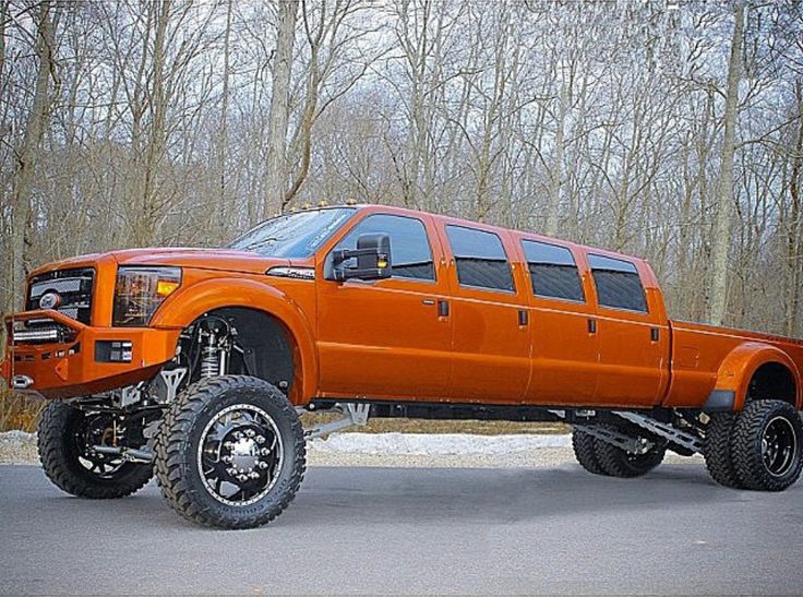 an orange lifted truck parked in front of some trees