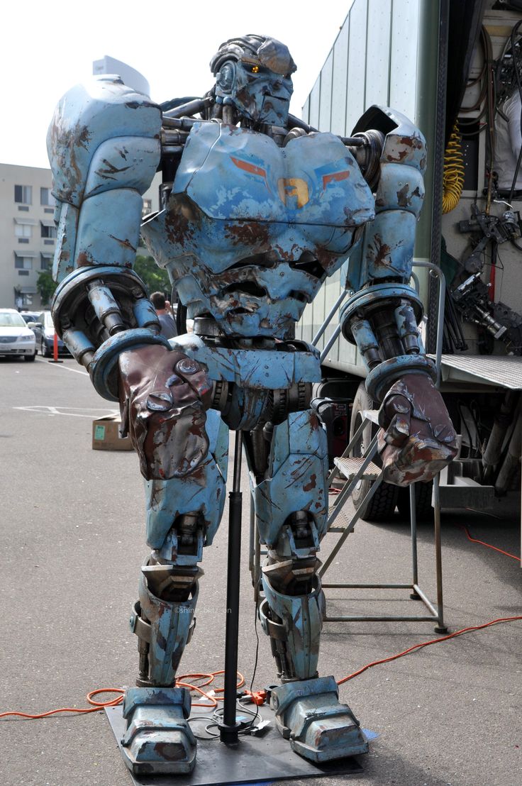 a blue robot statue sitting on top of a metal pole in the middle of a parking lot