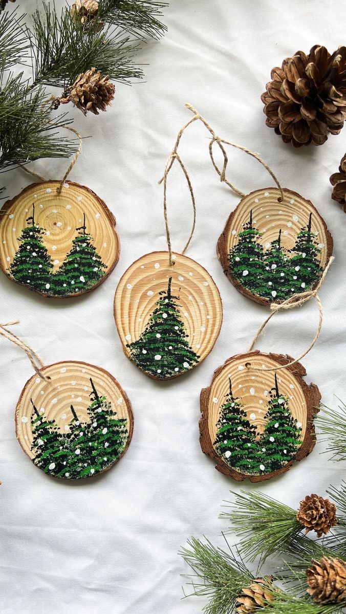 four wooden ornaments with trees on them and pine cones hanging from the tree branches in front of them