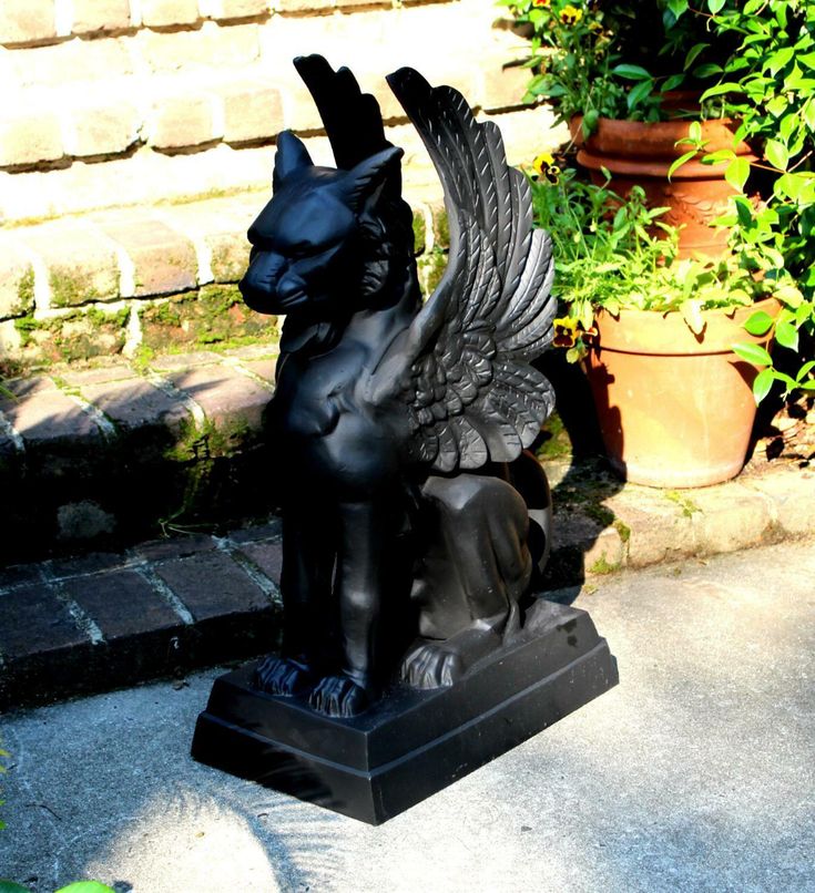 a statue of a dog with wings on it's back sitting in front of some plants