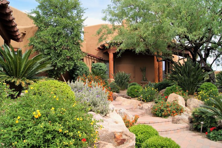 a garden with rocks, plants and trees in front of an adobe - style house