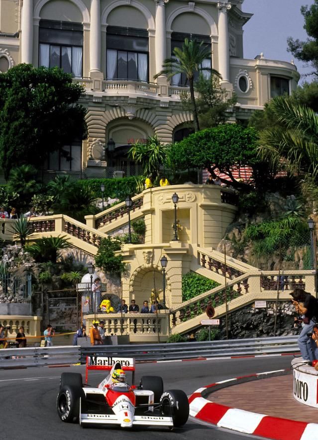 a man driving a race car down a street next to a tall building with stairs