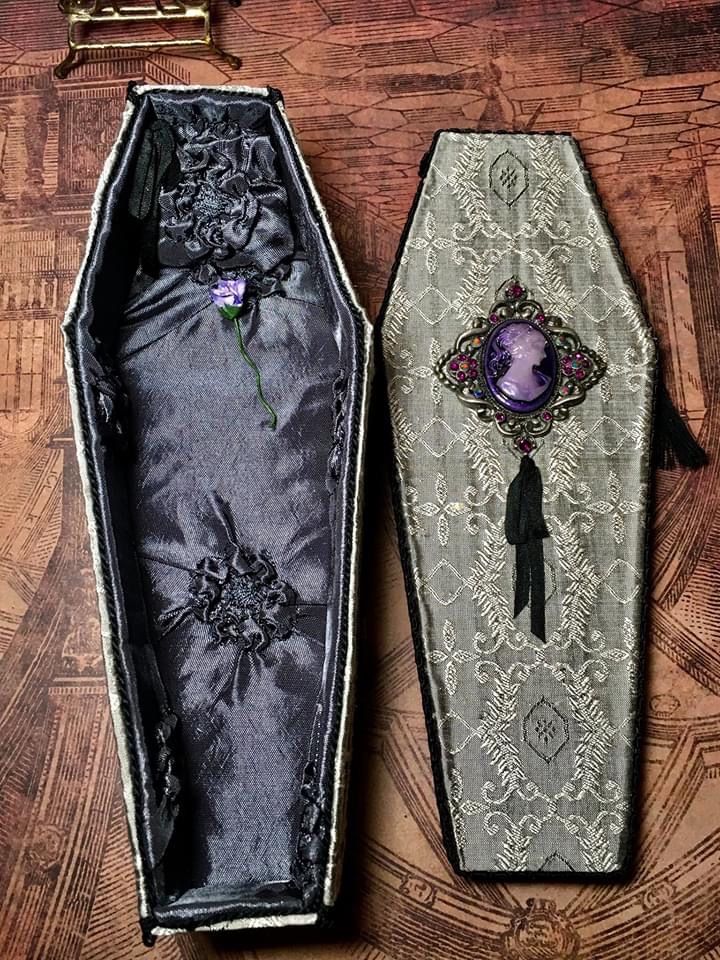 an open box with a purple brooch in it sitting on a wooden table next to another box