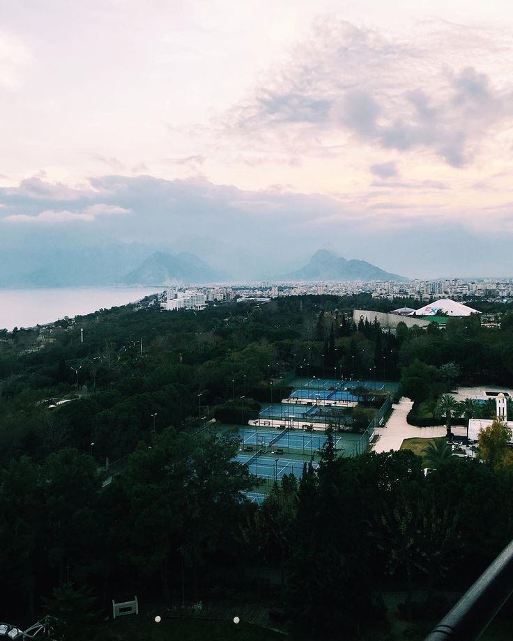 an aerial view of a tennis court surrounded by trees and mountains in the foreground