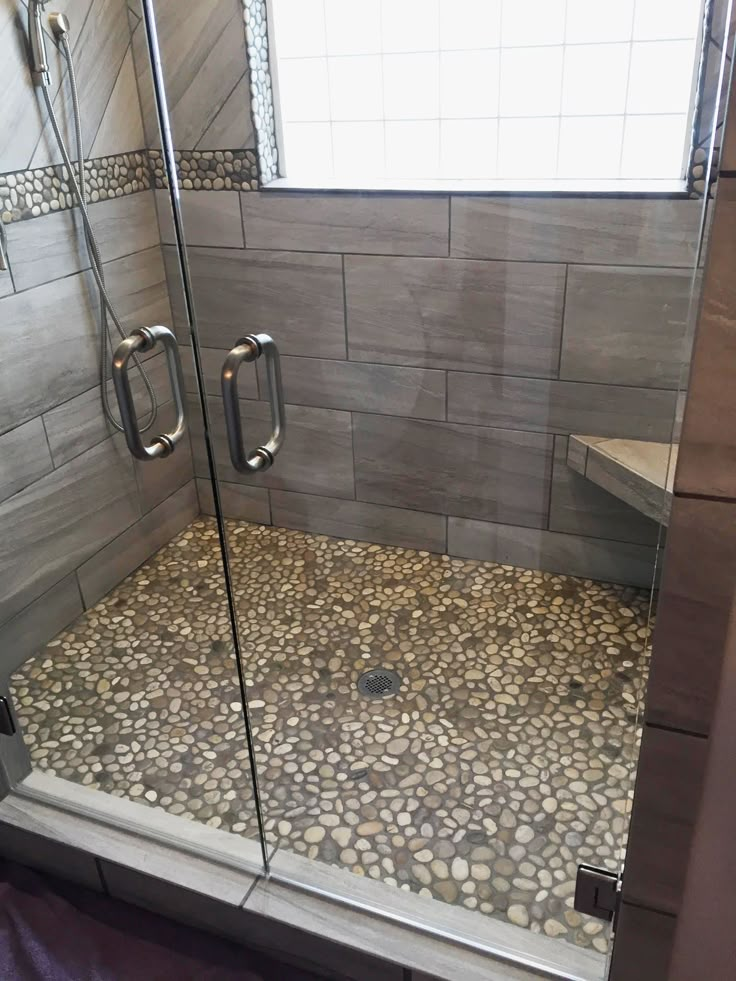 a walk in shower with rocks on the floor and glass doors to it's sides