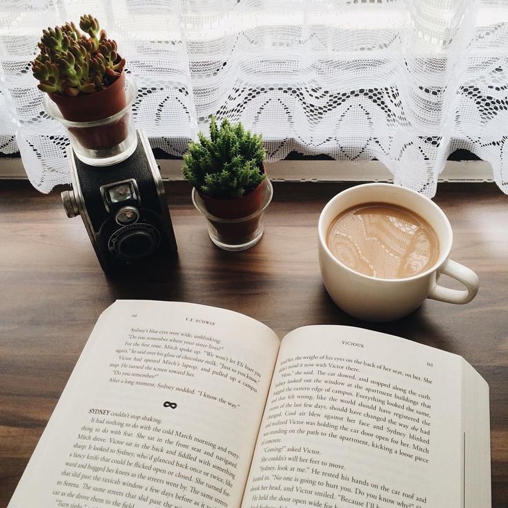 an open book sitting on top of a table next to a cup of coffee