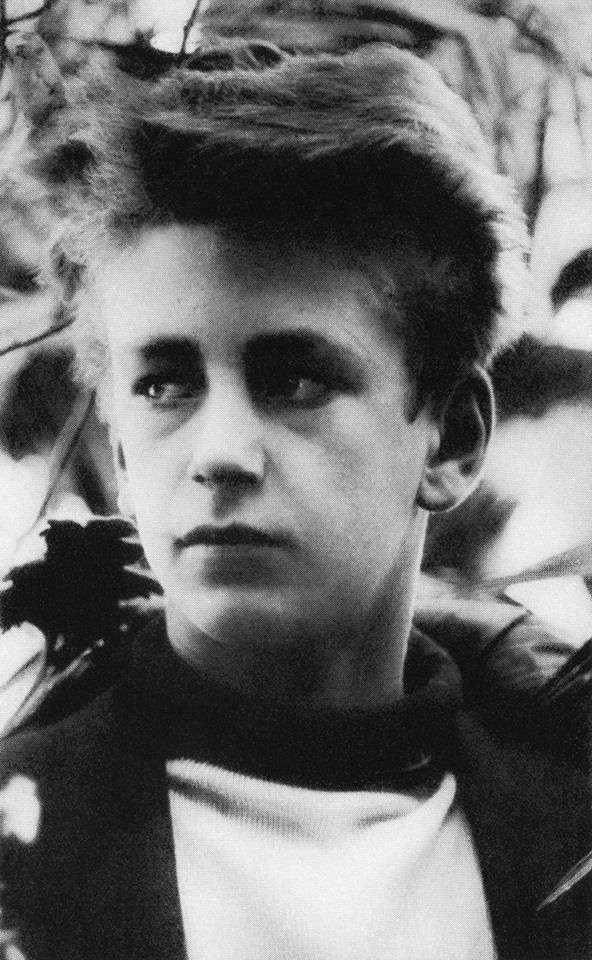 an old black and white photo of a young boy in front of a tree with leaves