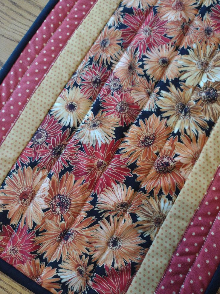 a quilted table runner with flowers and polka dots on the edge, sitting on top of a wooden table