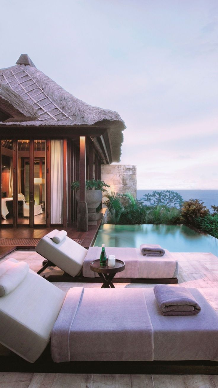 an outdoor living area with chaise lounges next to a pool and ocean view