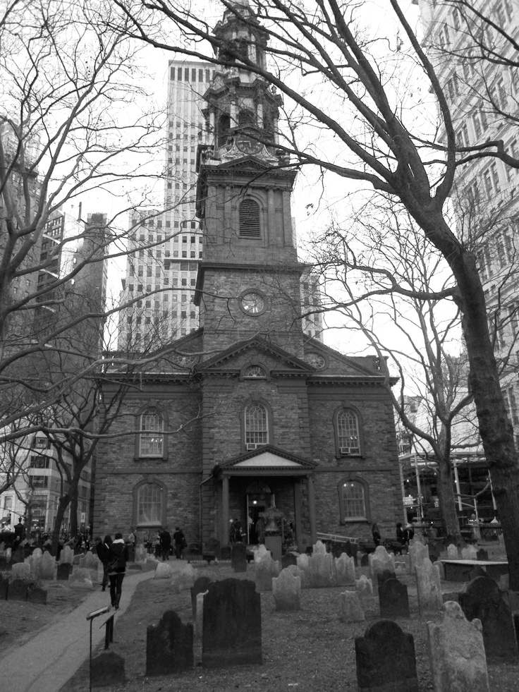 an old church in the middle of a cemetery surrounded by tall buildings and bare trees