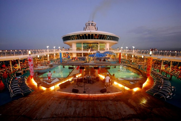 a cruise ship pool deck at night with people sitting on lounge chairs around the pool