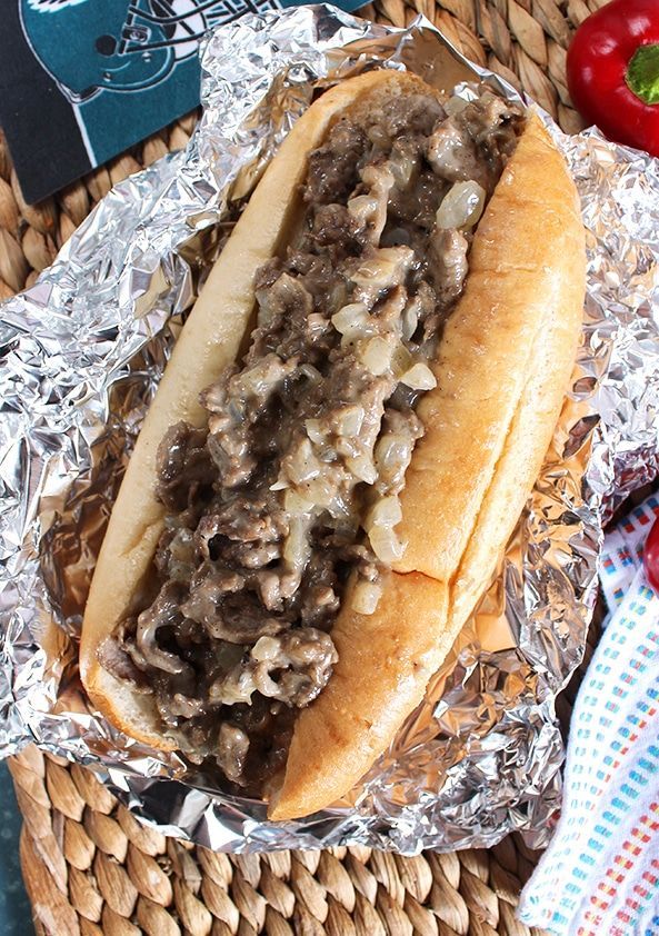 a hot dog covered in lots of meat on top of tin foil next to peppers