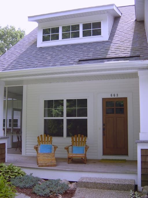 two chairs sitting on the front porch of a white house with wood doors and windows