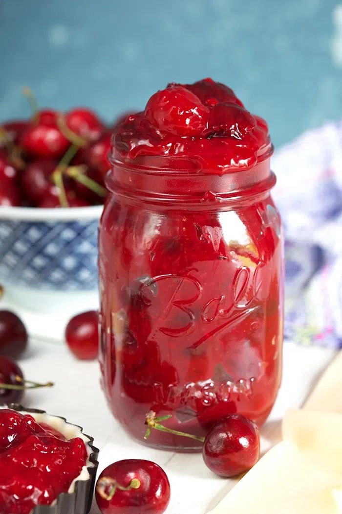 a jar filled with cherries next to muffins