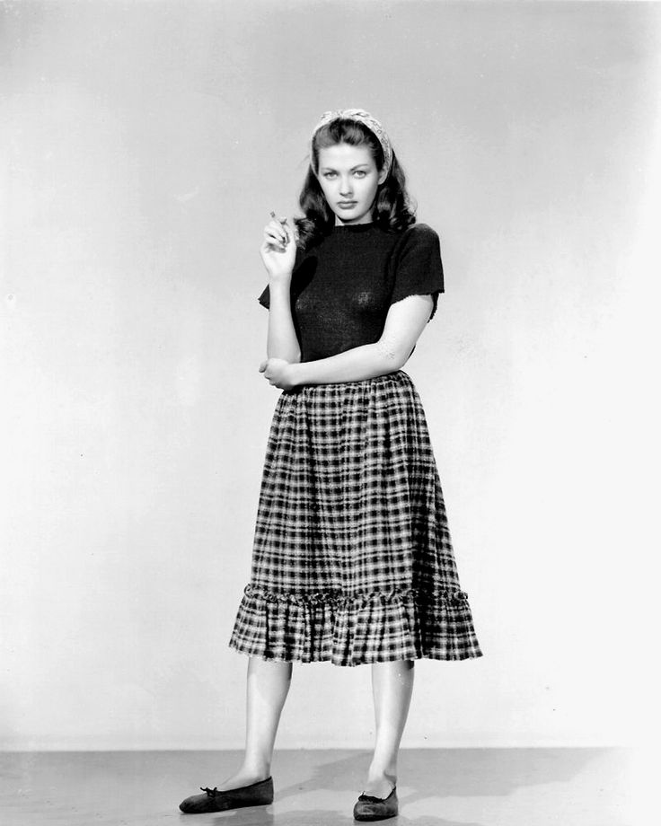 an old photo of a woman in a skirt and t - shirt posing for the camera