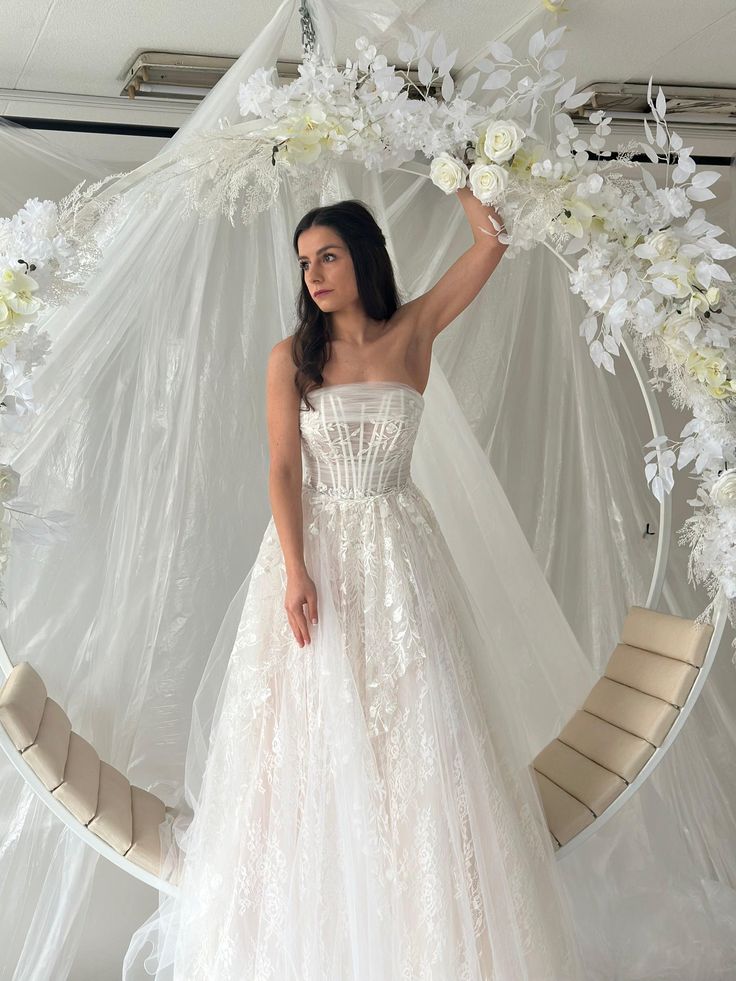 a woman standing in front of a white backdrop wearing a dress with flowers on it