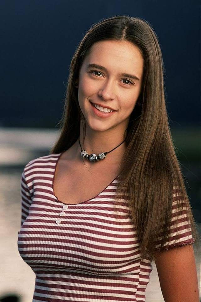 a woman with long brown hair wearing a striped shirt and necklace smiling at the camera