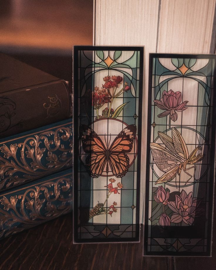 two stained glass panels sitting on top of a wooden table next to a bookshelf