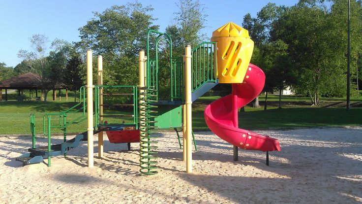 a colorful playground set in the middle of a sandy area with grass and trees behind it