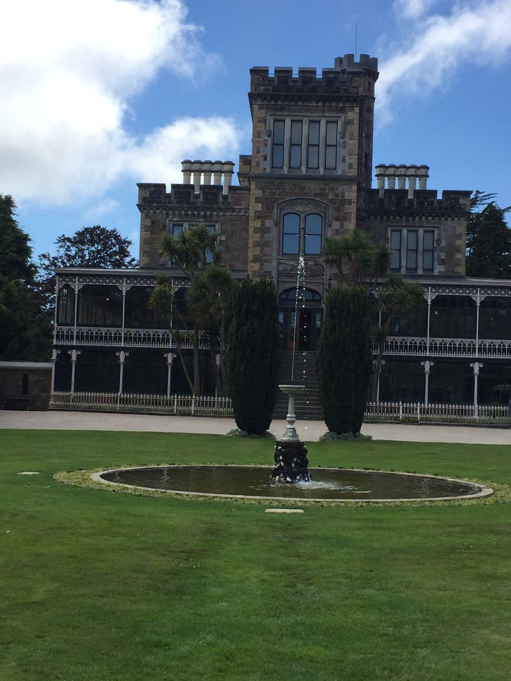 a large building with a fountain in front of it on a green lawn surrounded by trees