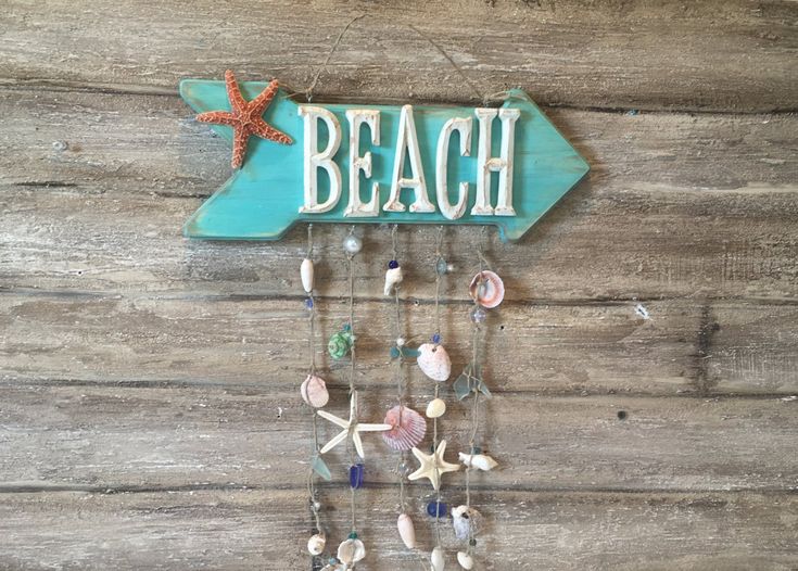 a wooden sign that says beach with shells and starfishs hanging from it's sides