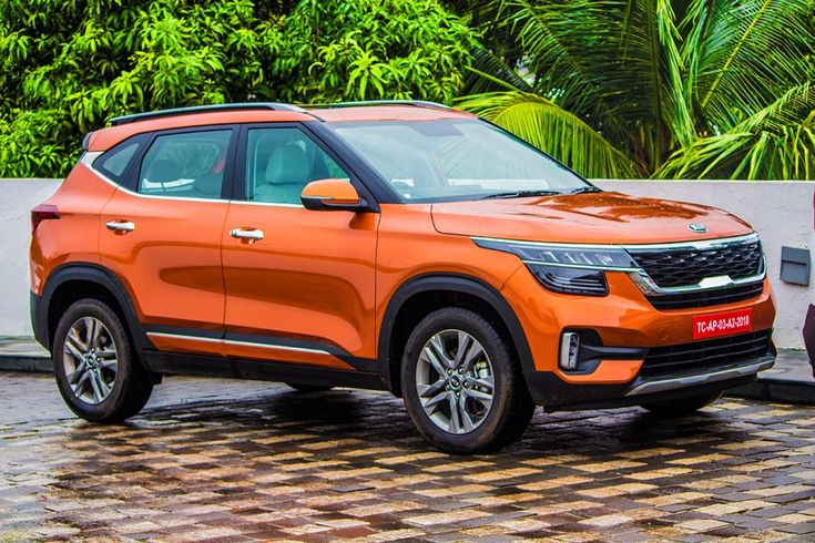 an orange suv is parked in front of a white wall and palm trees on the other side