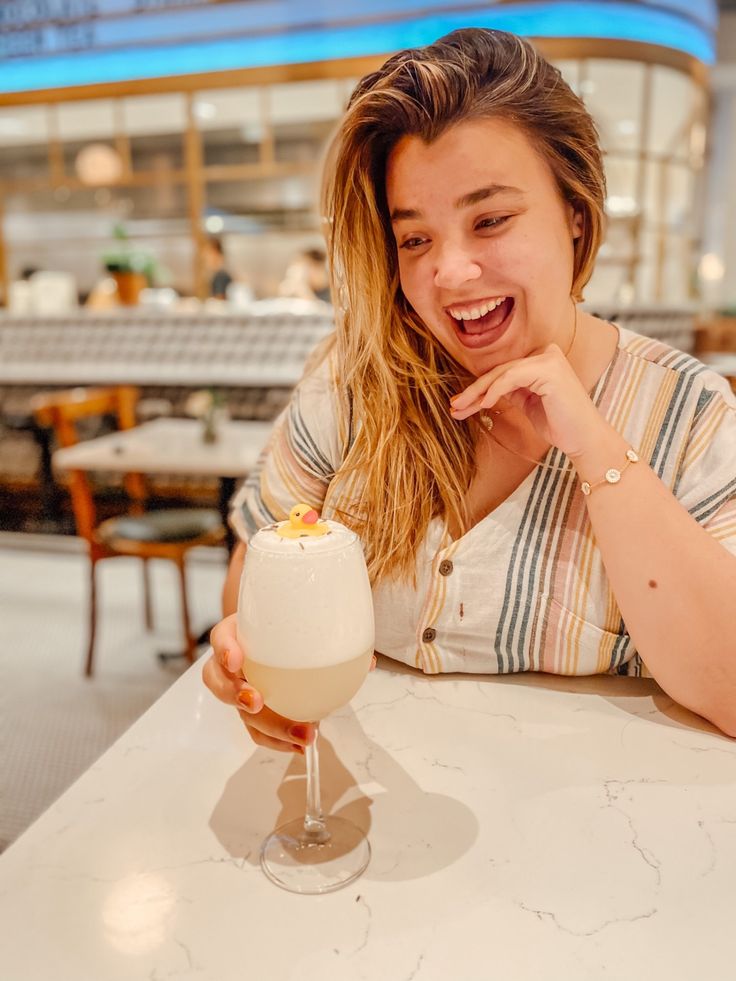 a woman sitting at a table with a drink in her hand and smiling for the camera