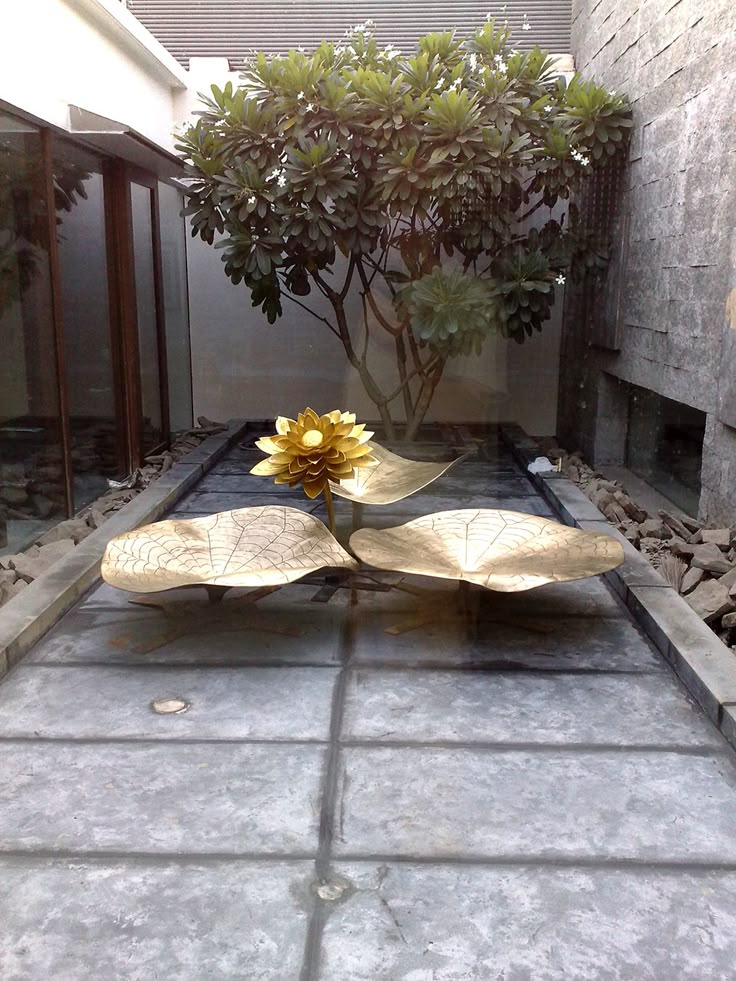 a large yellow flower sitting on top of a stone floor in front of a tree