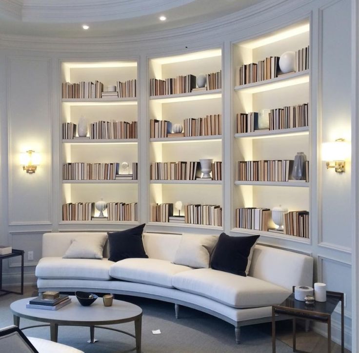 a living room filled with lots of white furniture and bookshelves on the wall