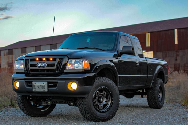 a black pickup truck parked in front of a building at dusk with its lights on