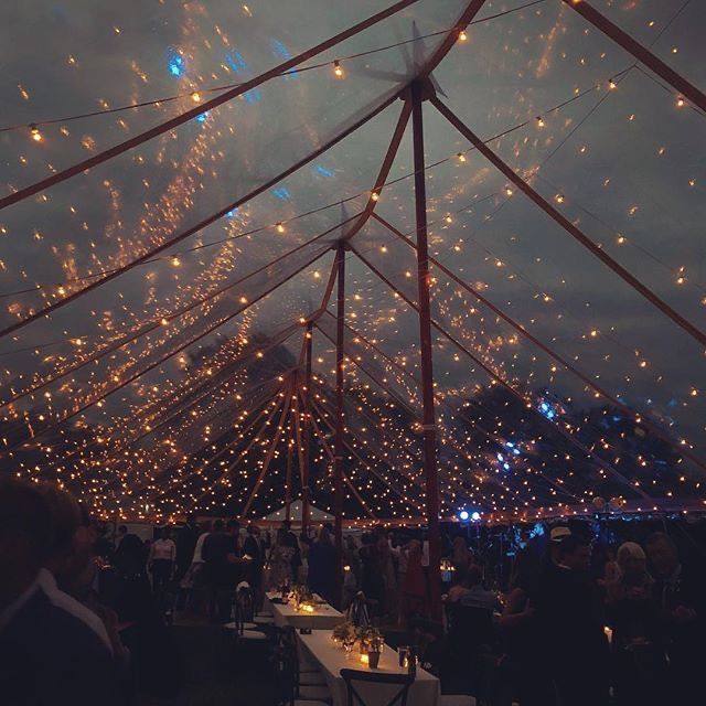 people sitting at tables under a tent covered in lights