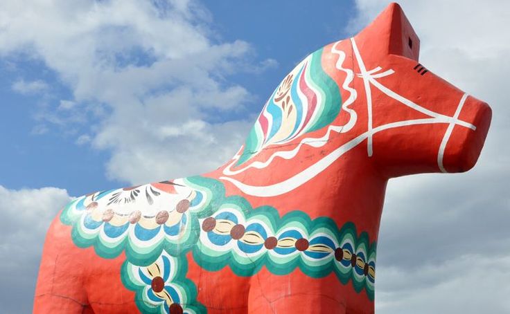 a large red horse statue sitting on top of a lush green field under a cloudy blue sky