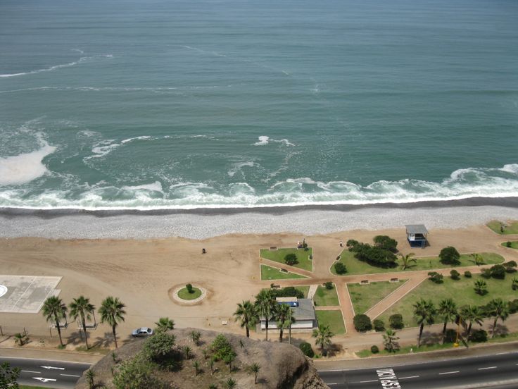 an aerial view of the beach and ocean with cars parked on the road next to it