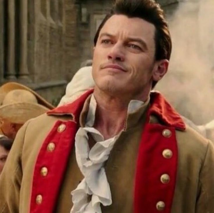 a man dressed in an old fashion outfit with red and gold trims is looking off to the side