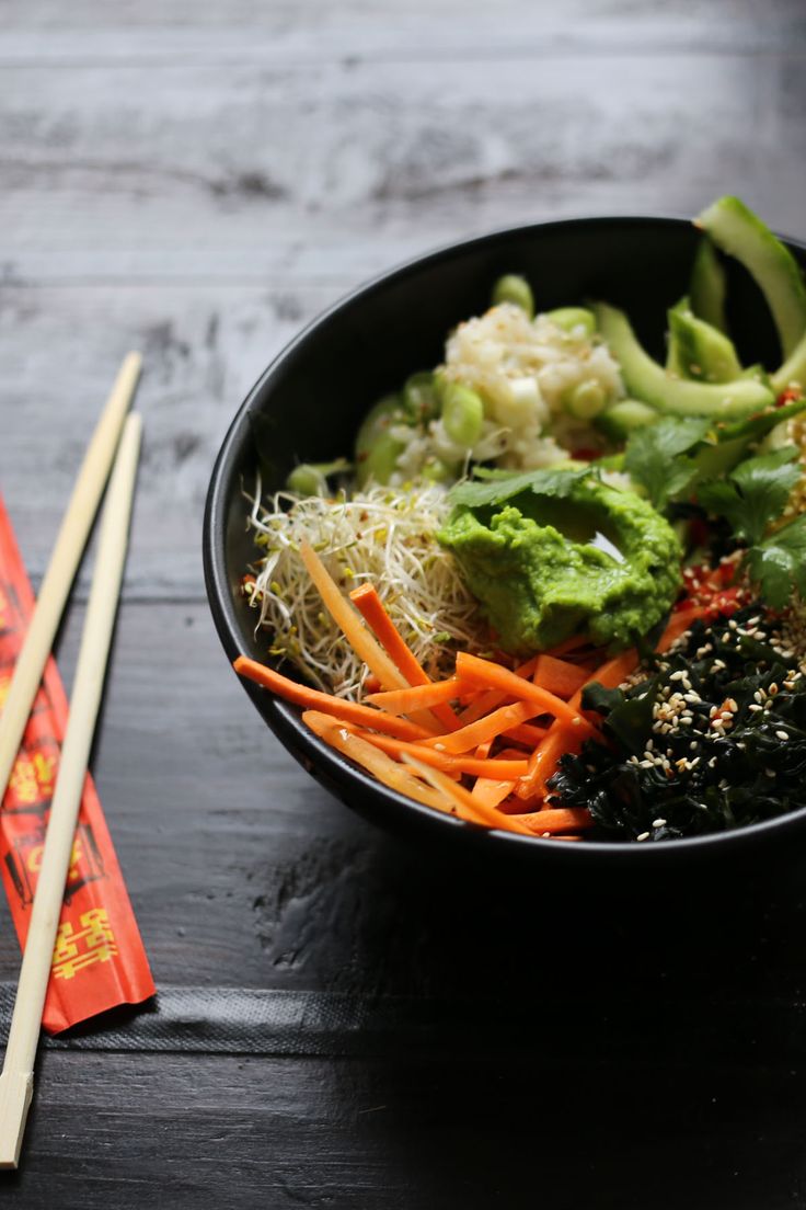 a black bowl filled with vegetables and chopsticks next to some broccoli