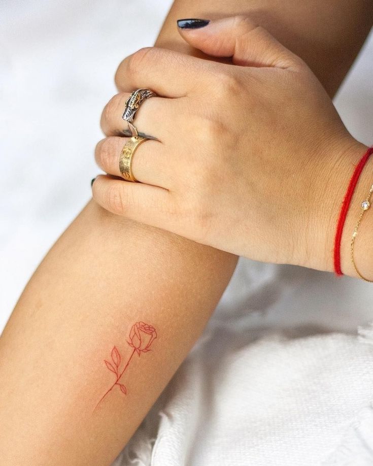 a woman's arm with a small red rose tattoo on the left side of her arm