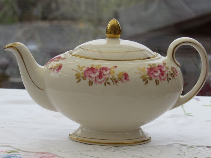 a white teapot with pink flowers on it sitting on a tablecloth covered table