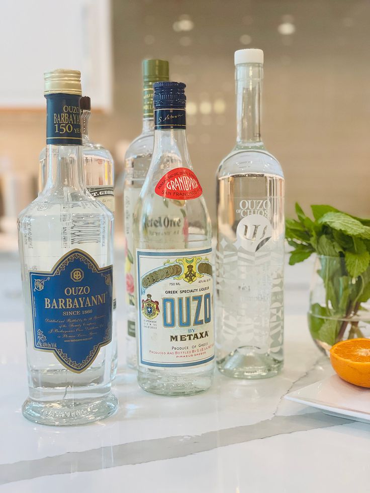 three bottles of alcohol sitting on top of a counter next to an orange and basil