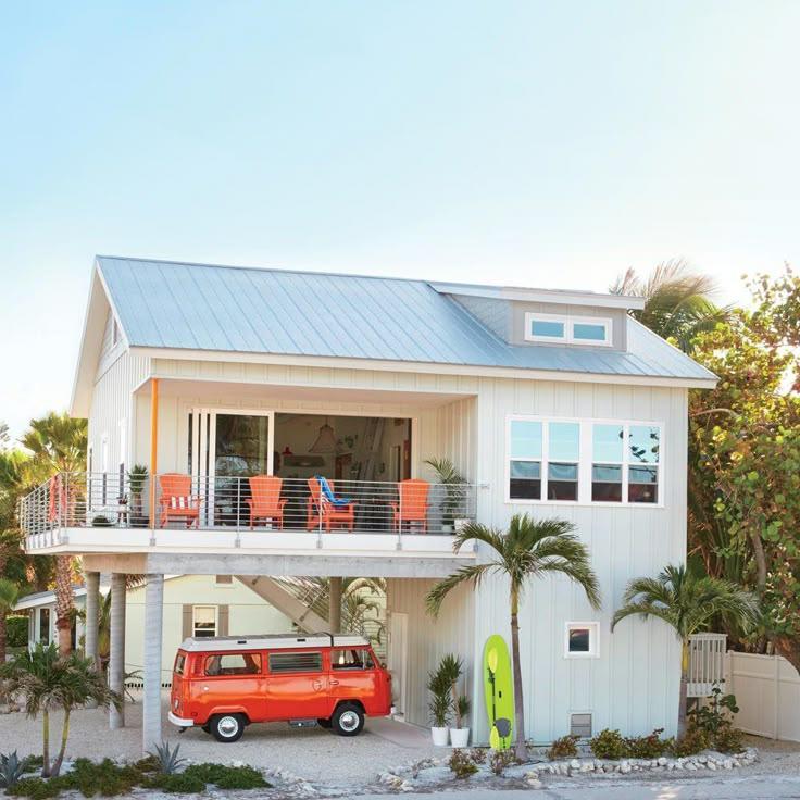 an orange van parked in front of a white house with a surfboard on the porch