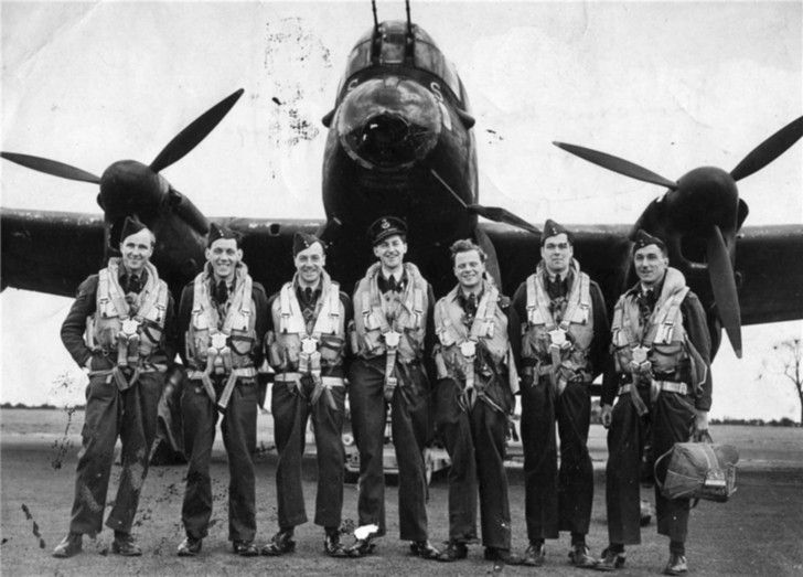 black and white photograph of pilots standing in front of an airplane