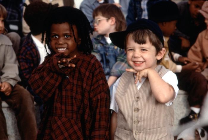 two young children are standing next to each other in front of a group of people