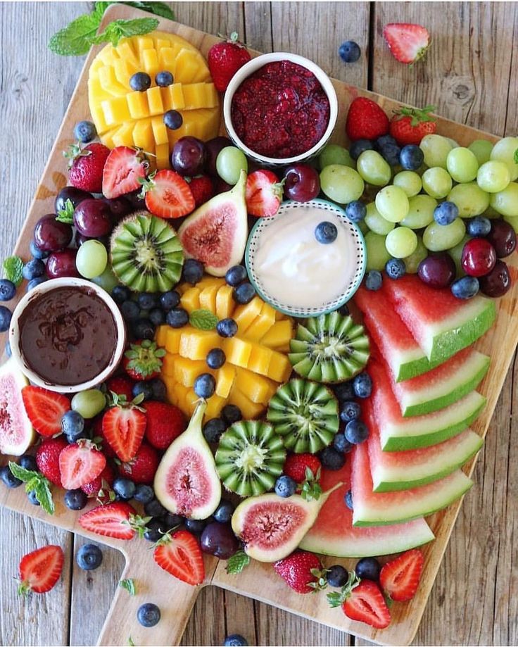 a wooden cutting board topped with fruit and dip