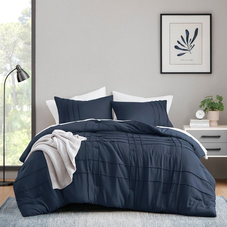 a bed with blue and white comforters in a room next to a window,