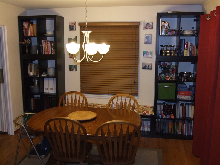 a dinning room table and chairs in front of a bookcase with books on it