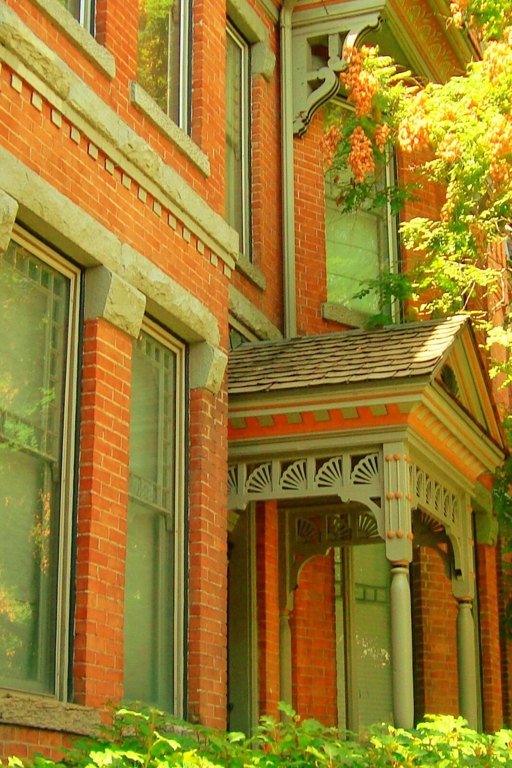 a red brick house with green trees in the front yard and an arched window on the second floor