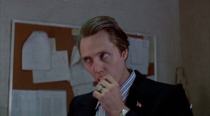 a man in a suit and tie eating something with his hand on his mouth while looking at the camera