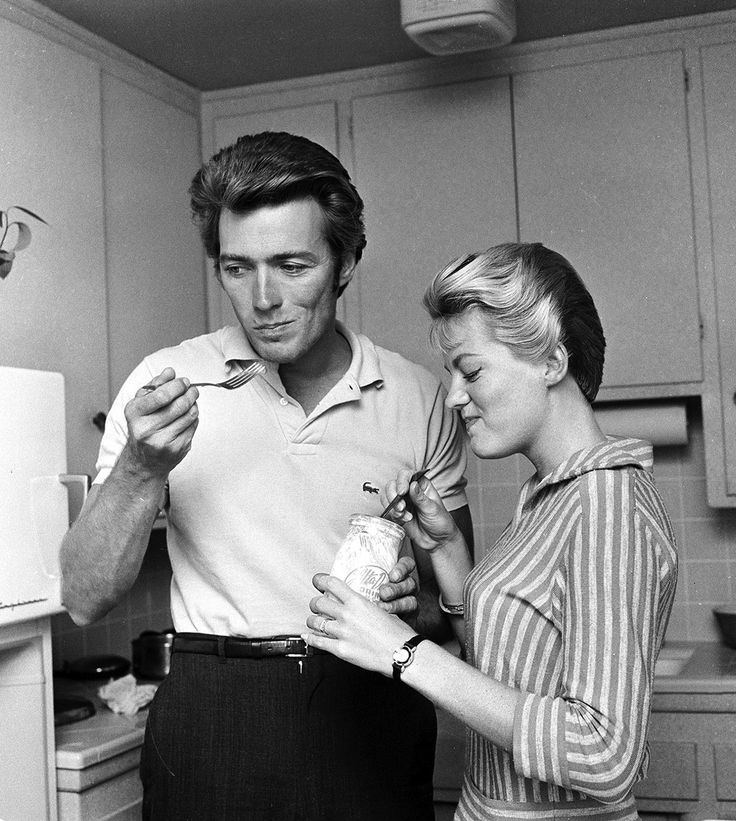 a man and woman are standing in the kitchen together, one is holding a bottle